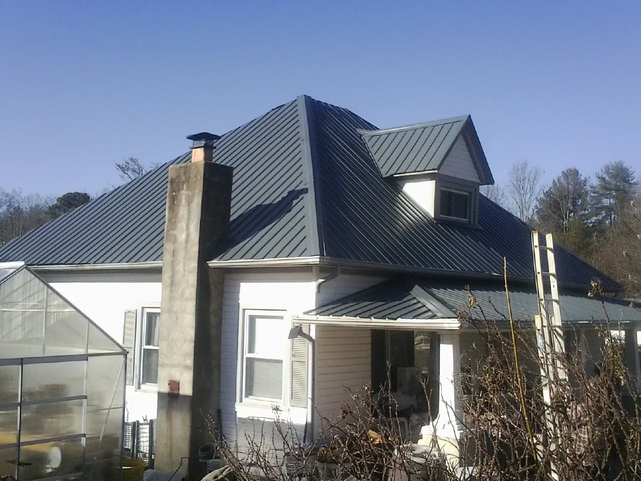 Dark blue standing seam metal roof on a white farmhouse with dormer — Slate & Tile Roof Repair by Roofing Brothers in West Harrison