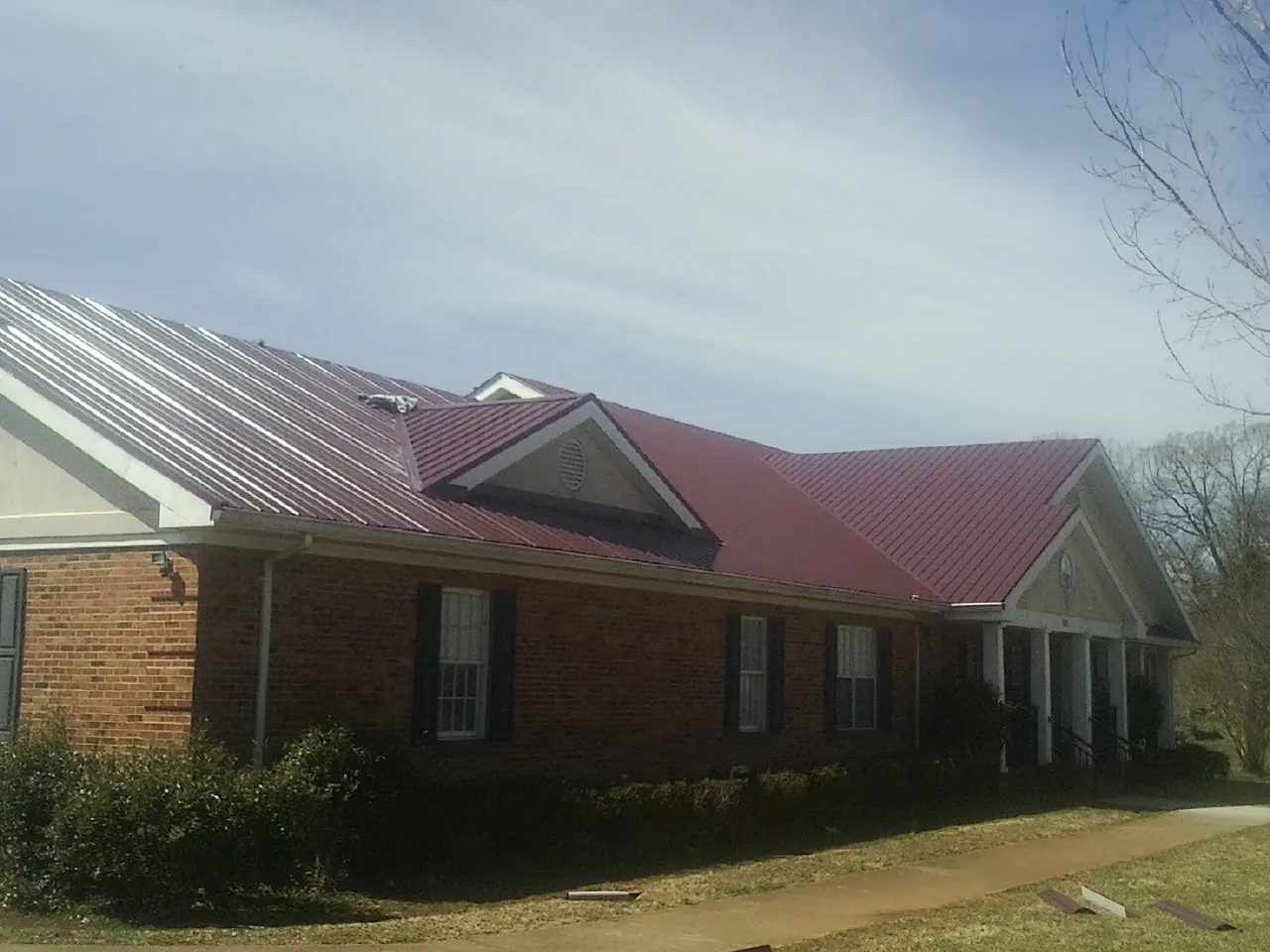 Red metal roof with gabled entries on a long brick building, from a Hail Damage Roof Repair job in West Harrison