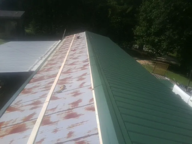Old rusted panels beside newly installed green metal roofing — Wind Damage Roof Repair by Roofing Brothers in West Harrison