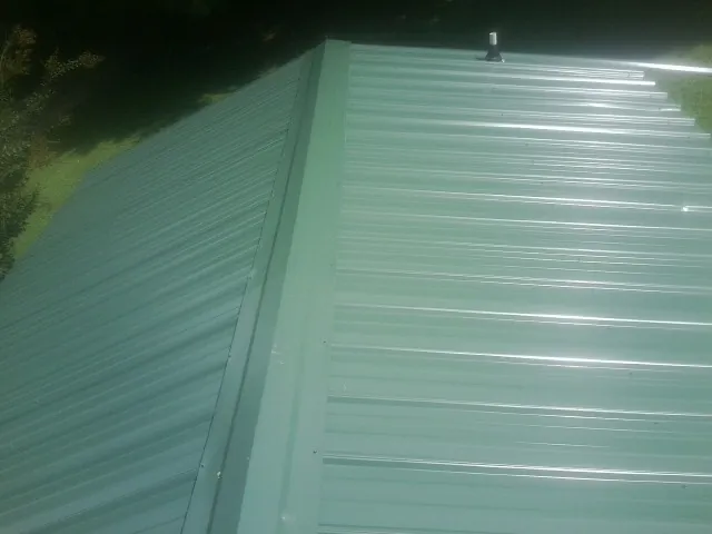 New green metal panels meeting at the ridge of a roof — Flat Roof Repair work by our crew in West Harrison