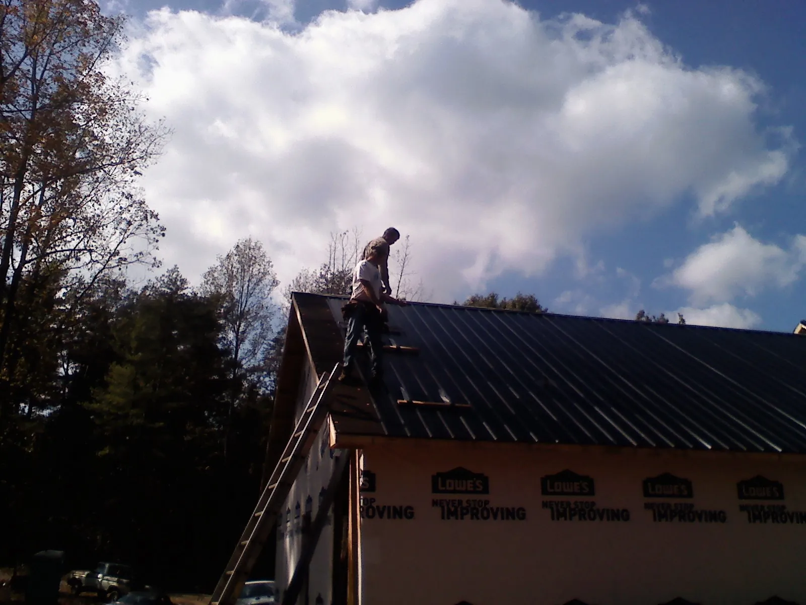 Roofer fastening dark metal panels high against a cloudy sky, from a Roof Inspection job in West Harrison