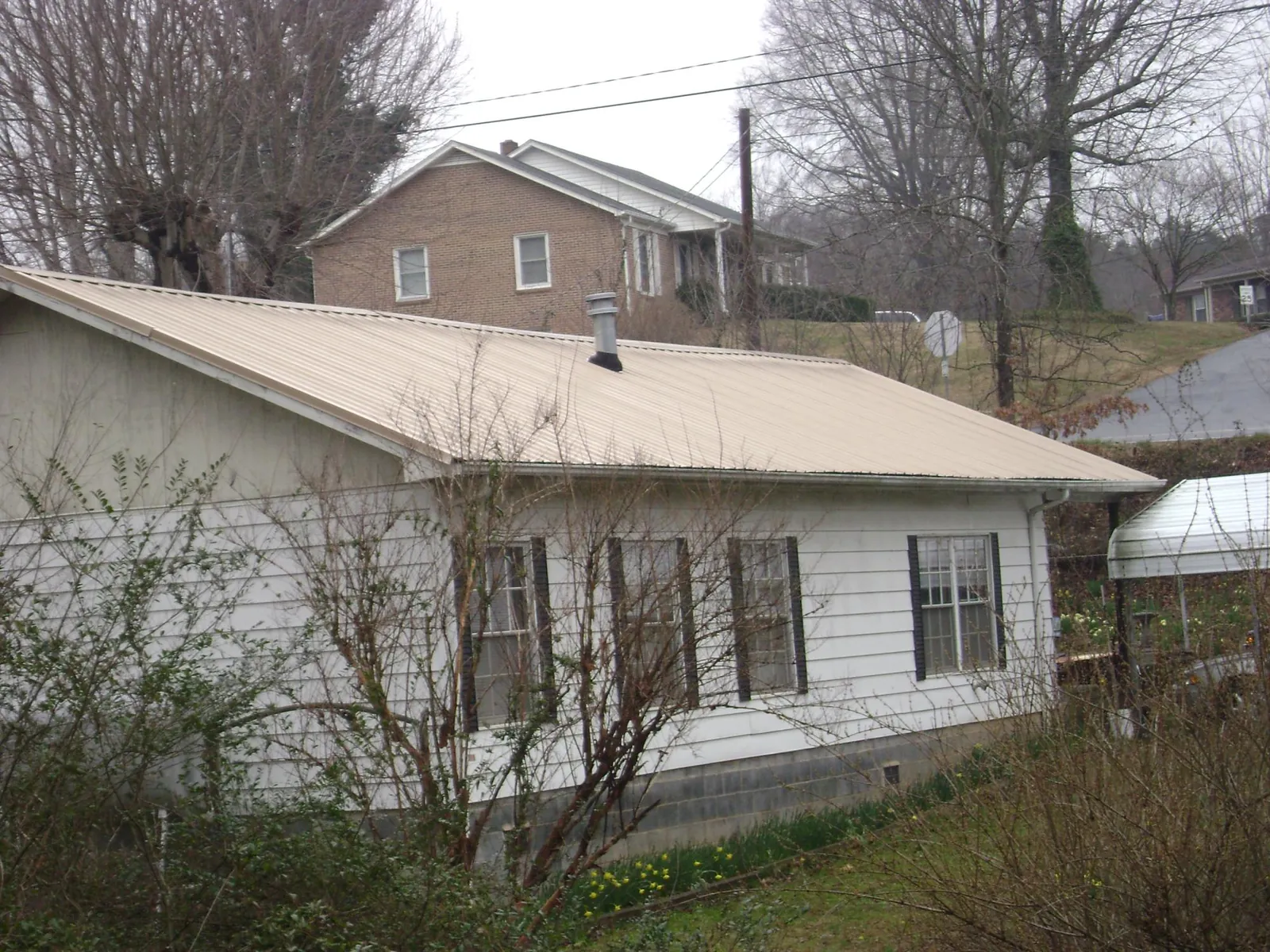 Tan metal roof on a white sided house set into a hillside — Commercial Roofing by Roofing Brothers in West Harrison
