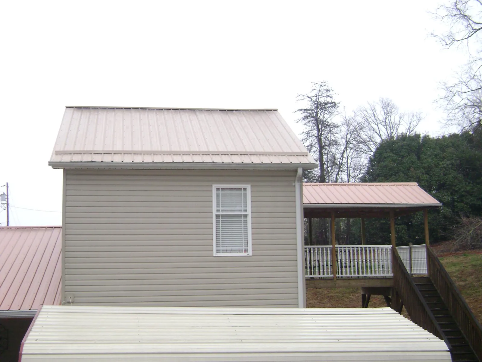 Tan metal roofs on a two story addition and attached porch, from a Roof Replacement job in West Harrison